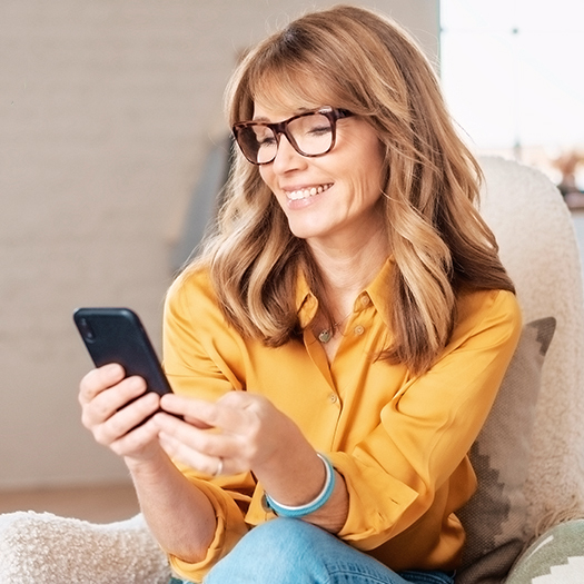 Women using their mobile phones and text messaging while relaxing at home in the armchair.