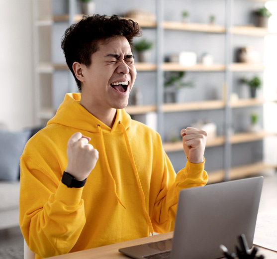 Young man celebrating while on his laptop