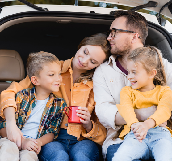 A young husband and wife with two children cozy in the truck of an SUV, admiring the fall season 