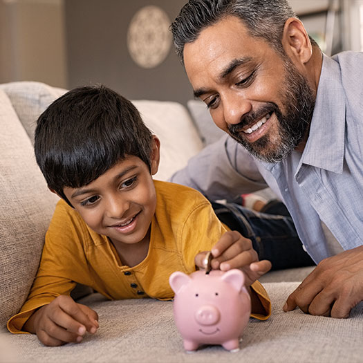 Son saving money in piggy bank with father