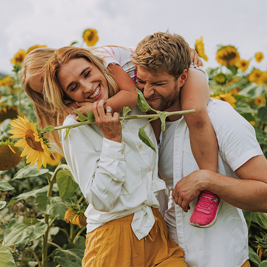 Young family laughing together in sunflower field in summer