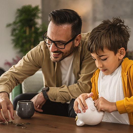 The father shows the son how to save money with a piggy bank at home.
