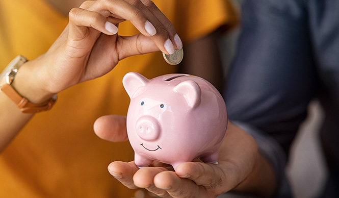 Close up of man holding pink piggy bank while woman putting coin in it.