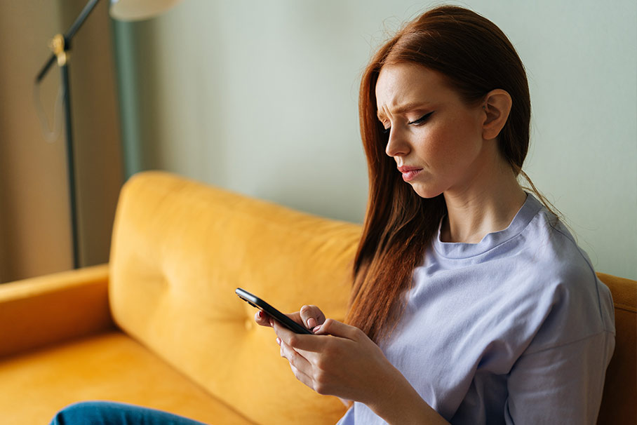 Woman sitting on her couch on her phone.