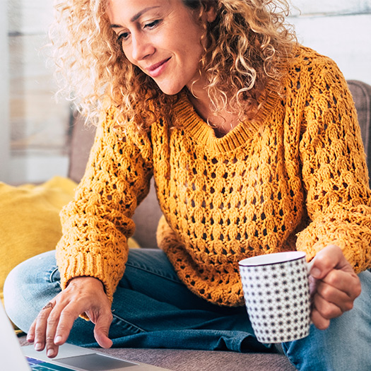 A lady with blonde curly hair working on a laptop on a sofa at home