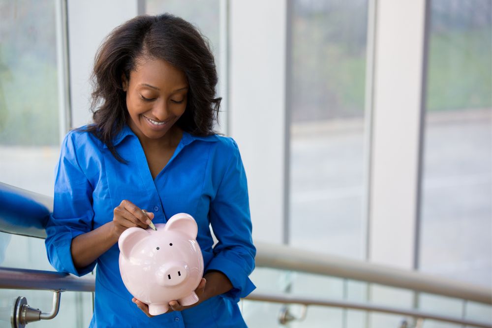 A woman holding a piggy bank while putting money in it.